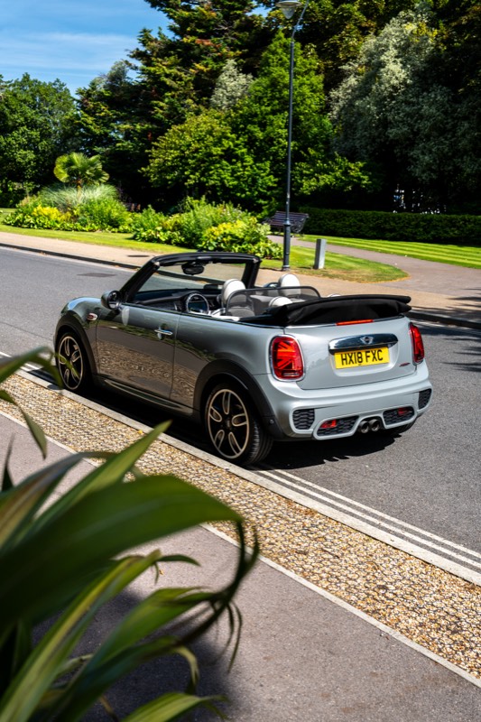 Silver MINI convertible with the roof down, parked beside gardens on a sunny road